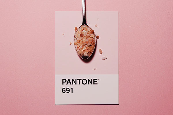 A spoonful of pink Himalayan salt rests on a Pantone 691 card, against a matching pink background.